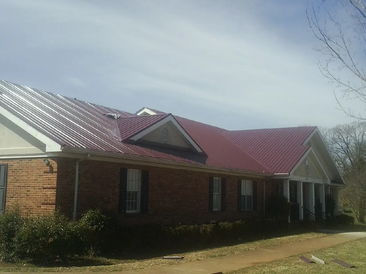 Red metal roof with gabled entries on a long brick building, from a Hail Damage Roof Repair job in Bethesda