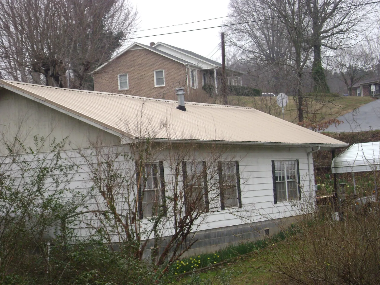 Tan metal roof on a white sided house set into a hillside — Commercial Roofing by Roofing Brothers in Bethesda